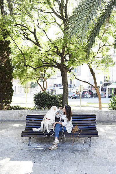 Junge Frau sitzt mit ihrem Hund auf der Bank in der Stadt