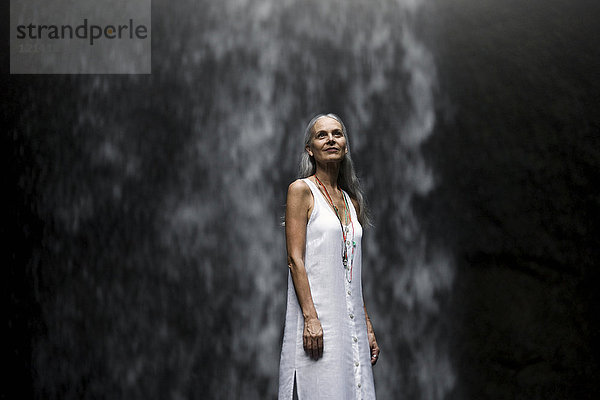 Schöne Seniorin vor einem tropischen Wasserfall stehend