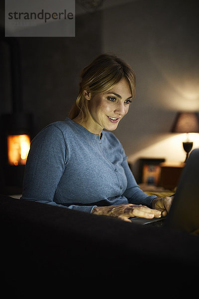 Porträt einer lächelnden Frau am Abend mit dem Laptop zu Hause
