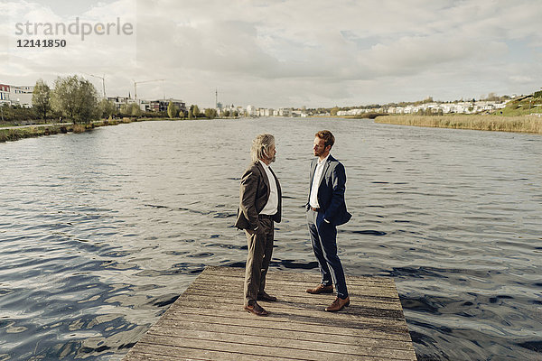 Zwei Geschäftsleute  die auf einem Steg am See stehen und reden.