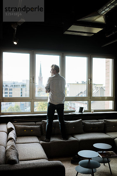 Geschäftsmann im Loungebereich eines Büros mit Blick aus dem Fenster