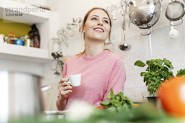 Lächelnde junge Frau mit Tasse Espresso in der Küche zu Hause
