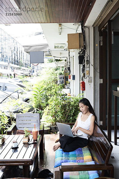 Frau mit Laptop auf Terrassenbank sitzend