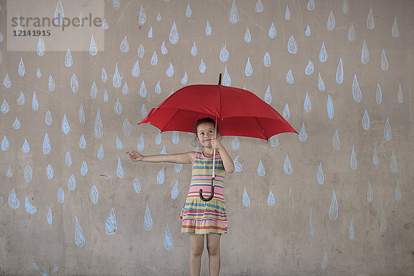 Mädchen mit einem roten Regenschirm neben einer Betonmauer mit Zeichnungen von Regentropfen.