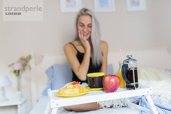 Lächelnde junge Frau beim Frühstück im Bett