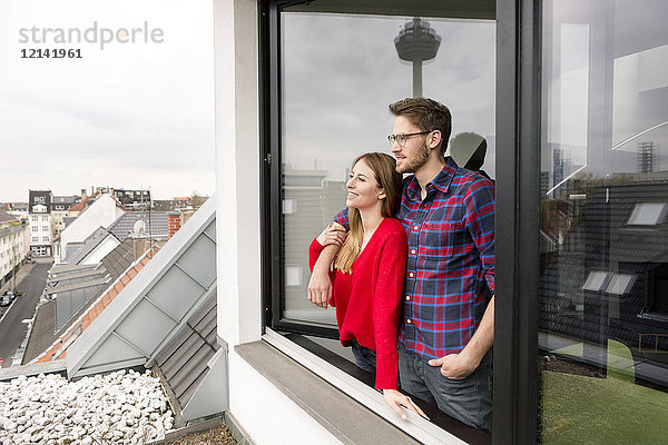 Lächelndes junges Paar schaut aus dem Fenster in der Stadtwohnung