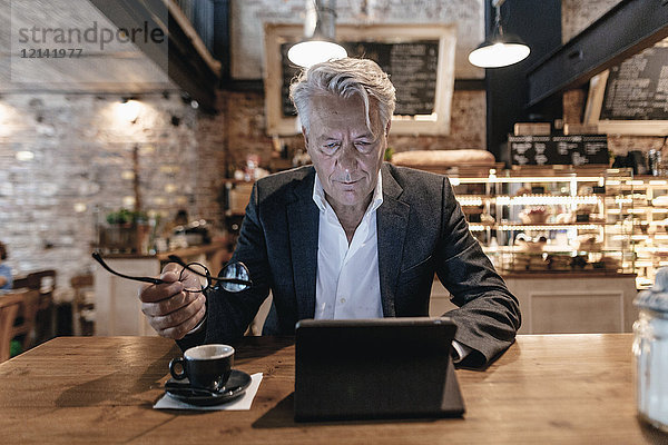 Senior Geschäftsmann sitzend im Cafe  mit digitalem Tablett  Lesen