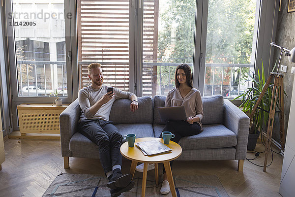 Paar sitzend auf Couch mit Handy und Laptop