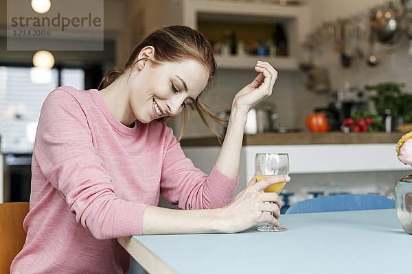 Lächelnde junge Frau mit einem Glas Orangensaft in der Küche zu Hause
