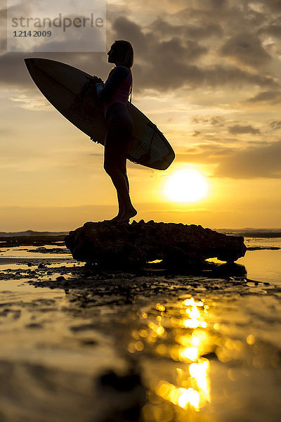 Indonesien  Bali  Silhouette einer jungen Frau mit Surfbrett gegen die Abendsonne