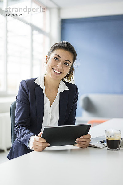 Porträt einer glücklichen Geschäftsfrau mit Tablette am Schreibtisch im Büro