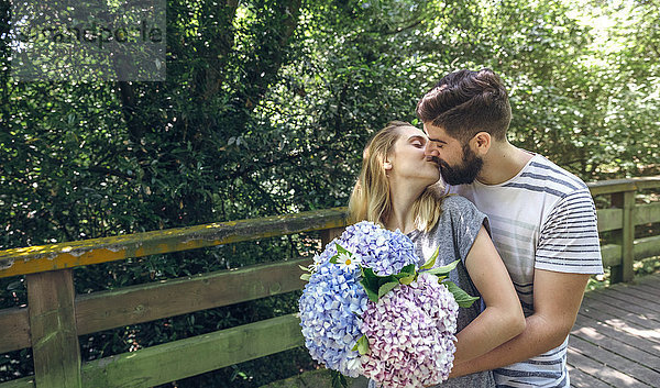 Paar mit einem Strauß Hortensien  die sich auf einem Holzsteg auf dem Land küssen.