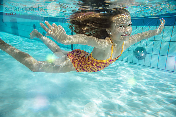 Porträt eines lächelnden Mädchens  das im Schwimmbad unter Wasser schwimmt.