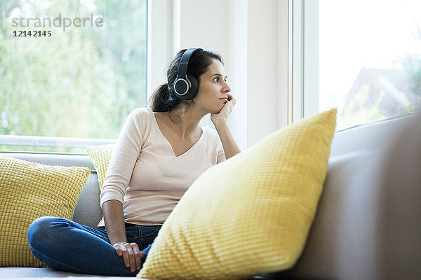 Frau sitzt allein auf der Couch und hört Musik mit Kopfhörern.