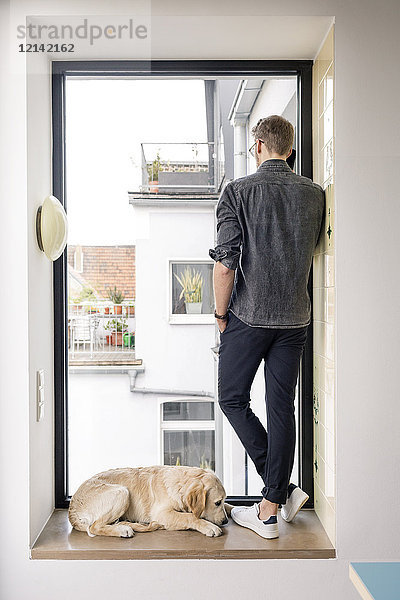 Mann am Telefon steht am Fenster neben dem Hund