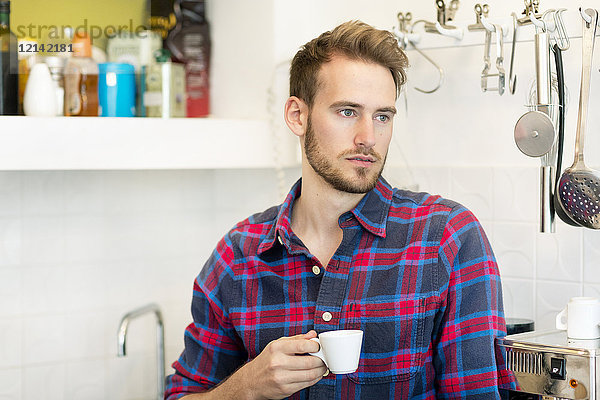 Nachdenklicher junger Mann mit Tasse Espresso in der Küche zu Hause