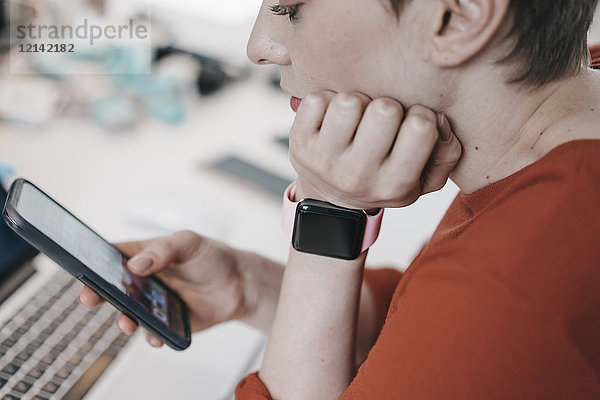 Frau trägt smartwatch mit Handy am Schreibtisch im Büro