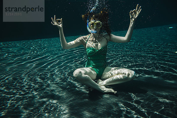Frau mit Taucherbrille und Schnorchel in Yoga-Pose unter Wasser im Schwimmbad