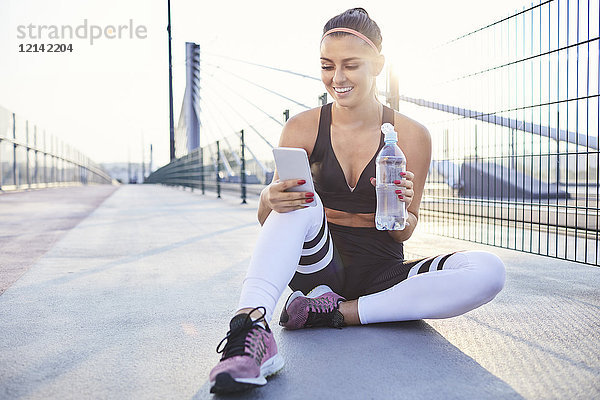 Sportlerin trinkt Wasser und überprüft ihr Handy nach dem Training