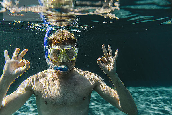 Porträt eines Mannes mit Taucherbrille und Schnorchel unter Wasser in einem Schwimmbad.