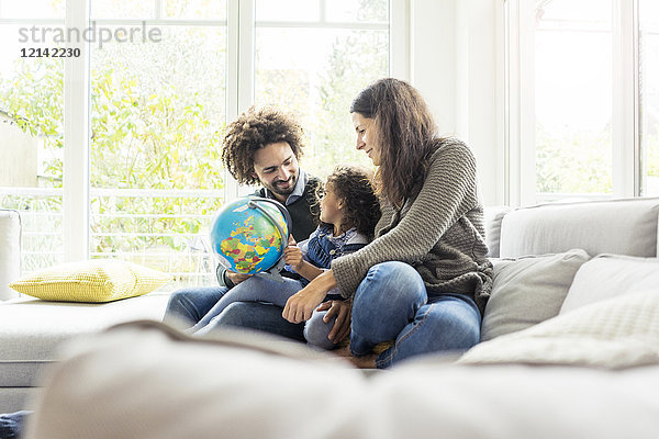 Glückliche Familie sitzend auf Couch mit Globus  Tochter lernt Geographie