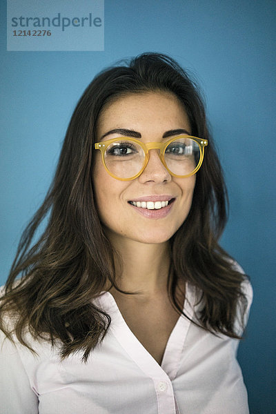 Porträt einer lächelnden Frau mit Brille vor blauem Hintergrund