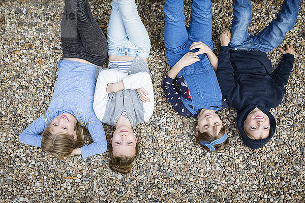 Drei Mädchen und ein Junge liegen auf dem mit Kieselsteinen bedeckten Boden.