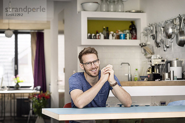 Porträt eines lächelnden jungen Mannes  der zu Hause am Küchentisch sitzt.