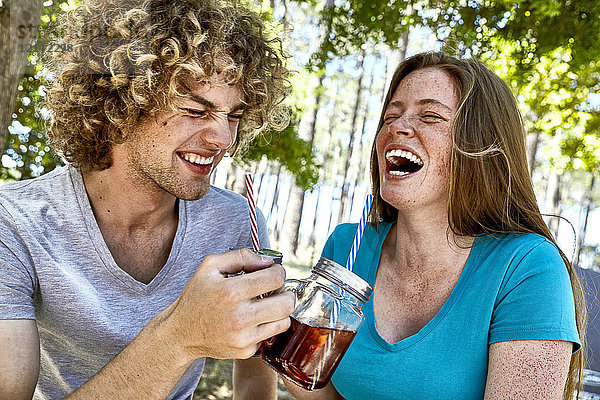 Lachendes junges Paar bei einem Drink im Wald
