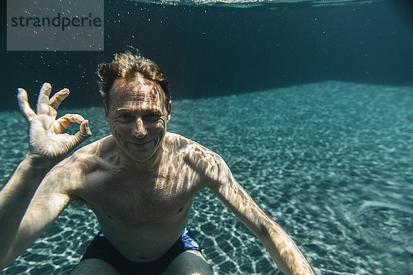 Porträt eines lächelnden Mannes unter Wasser in einem Swimmingpool mit ok-Schild