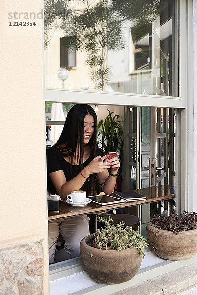 Lächelnde Asiatin beim Telefonieren in einem Café am Fenster