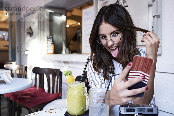 Junge Frau sitzt in einem Coffee-Shop und nimmt Selfie mit Smartphone