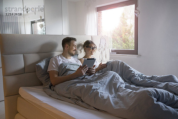 Lächelndes Paar im Bett zu Hause mit Tabletten