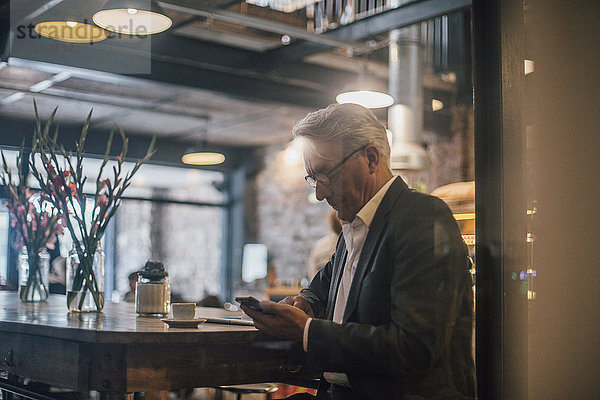 Senior Geschäftsmann sitzt im Cafe  mit Smartphone