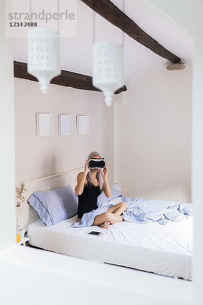 Junge Frau im Bett sitzend mit VR-Brille