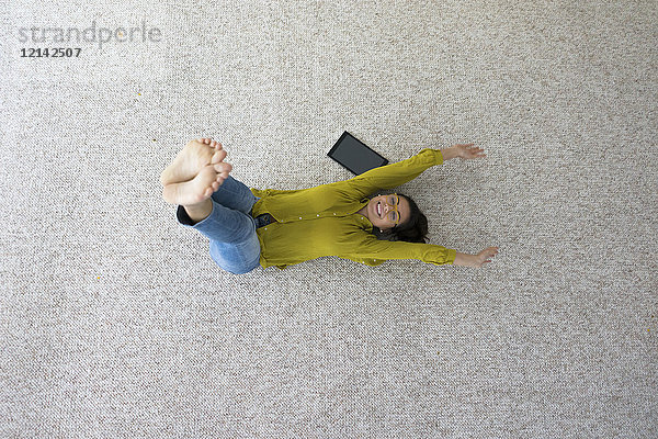 Lachende Frau auf dem Teppich liegend bei Dehnübungen  Draufsicht
