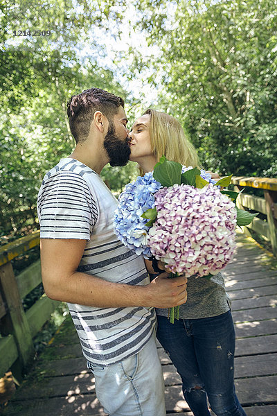 Paar mit einem Strauß Hortensien  die sich auf einem Holzsteg auf dem Land küssen.