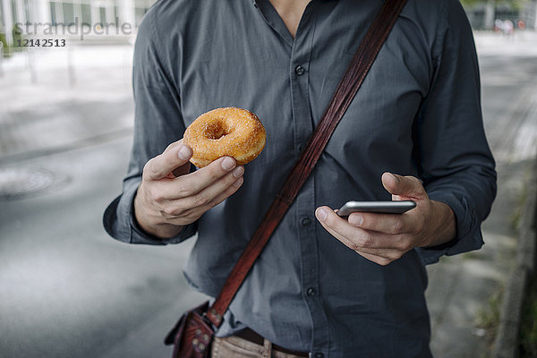 Hände des Geschäftsmannes mit Donut und Smartphone  Teilansicht