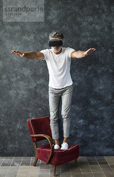 Der reife Mann schaut durch die VR-Brille und balanciert auf dem Sessel.
