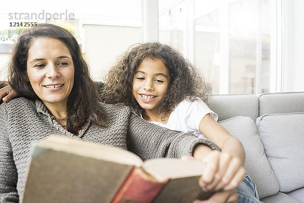 Mutter und Tochter sitzen auf der Couch und lesen ein Buch.