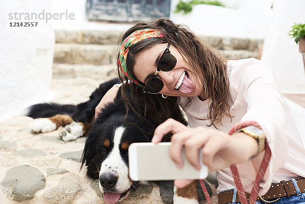 Brünettes Mädchen nimmt Selfie  müde Berner Sennenhund auf dem Boden liegend