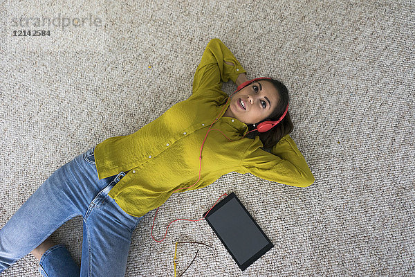 Porträt einer auf dem Boden liegenden jungen Frau mit Kopfhörer und Tablett Musik hören  Draufsicht