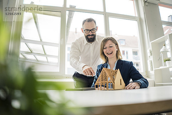 Lachende Frau und Mann mit Hausmodell im Büro