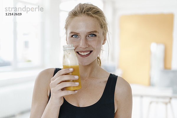 Porträt einer lächelnden jungen Frau in Sportbekleidung  die einen Smoothie trinkt.