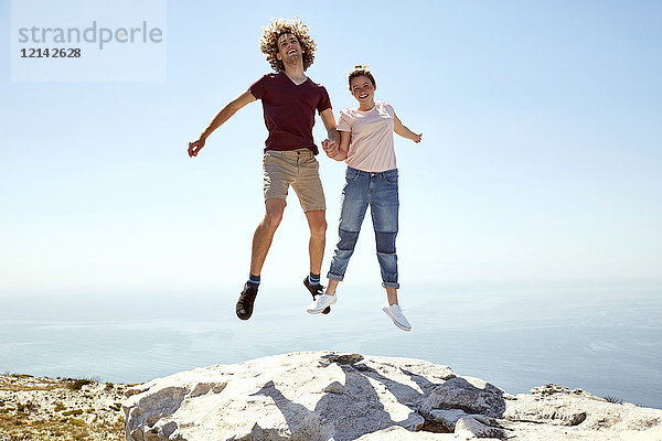 Südafrika  Kapstadt  glückliches junges Paar  das auf einen Berg an der Küste springt.