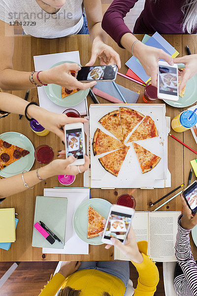 Gruppe junger Frauen zu Hause  die Handyfotos machen und sich eine Pizza teilen.
