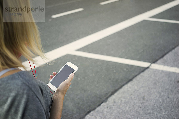 Junge Frau mit Handy am Straßenrand  Teilansicht
