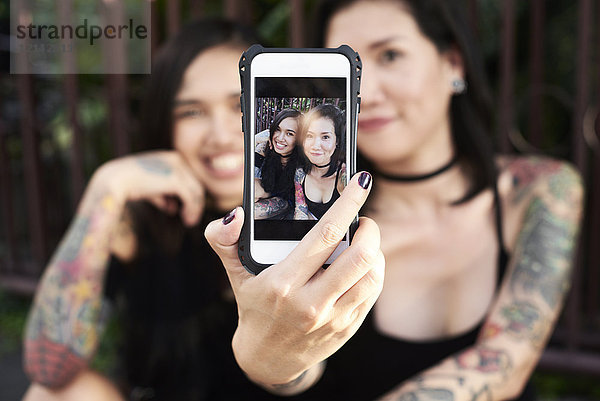 Frau hält Handy mit Selfie von sich und ihrer lesbischen Partnerin