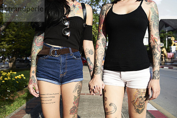 Tätowiertes lesbisches Paar  das im Sommer auf der Straße Händchen hält.