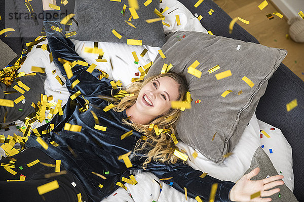 Porträt einer glücklichen jungen Frau mit fliegenden Konfetti zu Hause